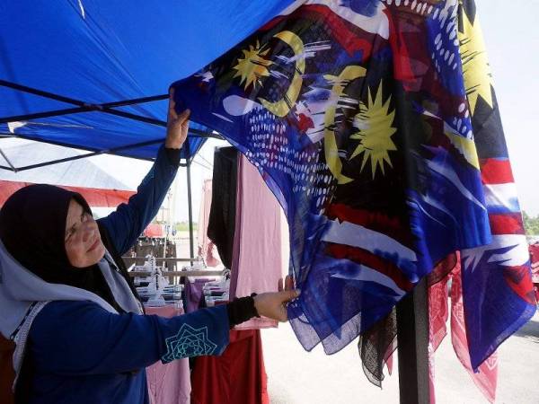 Hamidah menunjukkan tudung bercorak Jalur Gemilang yang dijual di gerainya di pekan sehari Pendang, Kedah hari ini.