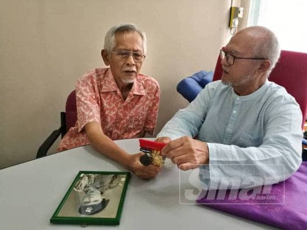 Khairuddin (kanan) menunjukkan pingat dan gambar lama kepada Mohd Ghazali.
