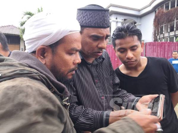 Abdul Kadir (tengah) menunjukkan gambar mangsa kepada rakannya.