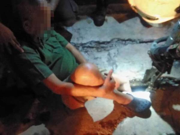 Anggota bomba berusaha mengeluarkan kaki kiri mangsa yang tersepit batu penutup longkang dalam kejadian di Kampung Bunga Paya Pantai awal pagi tadi. - Foto JBPM