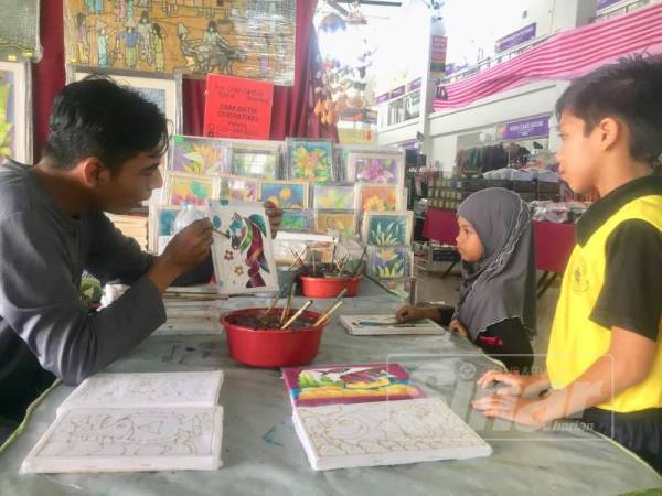 Kanak-kanak turut diajar cara mewarna lukisan batik oleh peniaga di Serambi Teruntum.