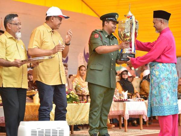 Tengku Muhammad Ismail (dua dari kanan) menyampaikan piala pusingan kepada wakil MBKT yang muncul sebagai johan keseluruhan pertandingan perbarisan. - Foto UPDI