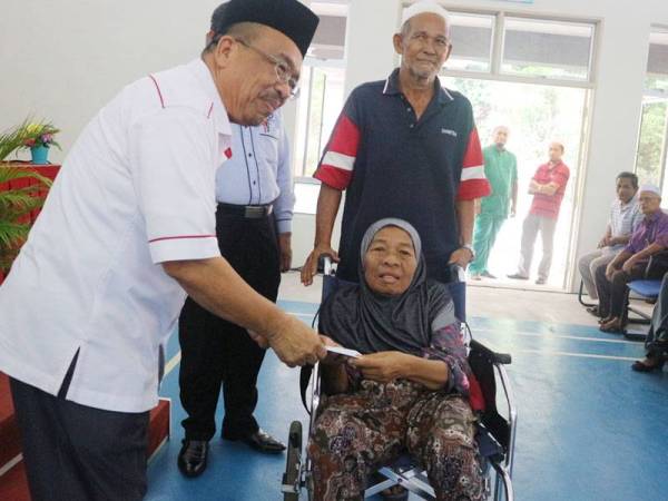 Phahrolrazi menyampaikan zakat kepada Indun yang berkerusi roda sambil diperhatikan suaminya, Azmi pada Program Kasih Peladang Kedah PPK Lubuk Batu di sini semalam.