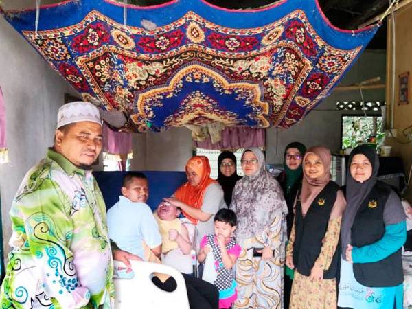 Abdullah (kiri) menyerahkan katil khas kepada keluarga ini di kediaman mereka di Kampung Lebur Jaya, Kuala Betis.