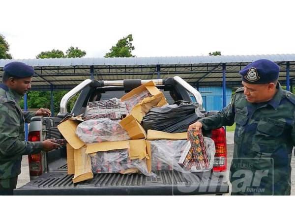 Azhari (kanan) memeriksa rokok yang berjaya dirampas pada sidang media di Markas Taktikal PGA, Lubok Stol hari ini.