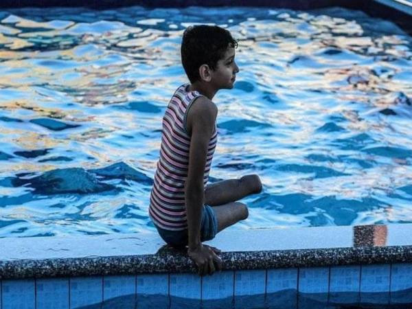 Seorang kanak-kanak yang kehilangan kedua-dua kaki sedang mandi di kolam renang.