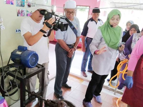 Afiqah (kanan) memberi penerangan proses pembuatan aiskrim kepada pelancong yang datang ke Tanjung Piai.