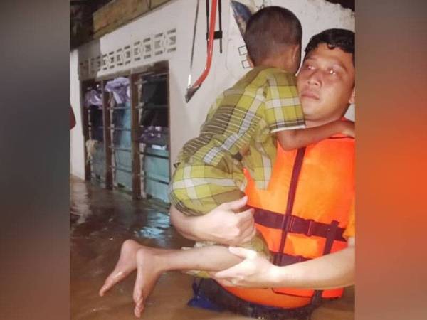 Seorang kanak-kanak dibantu anggota APM Baling selepas rumahnya dilanda banjir.