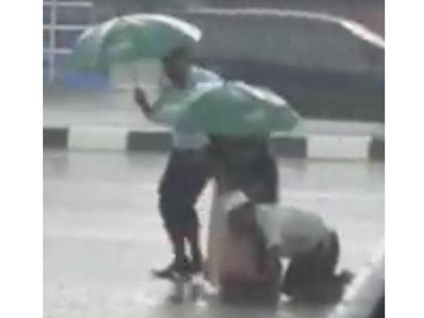 Wanita dan seorang lelaki yang mengangkat seorang warga emas ke tempat berbumbung untuk berlindung daripada hujan.