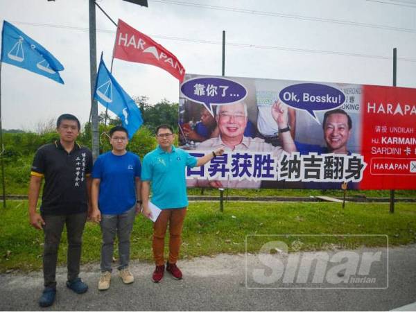 Tian Soon (kanan) bersama Zhi Li (tengah) menunjukkan papan iklan yang jelas melanggar syarat berkempen ditetapkan SPR di Pekan Nanas hari ini. - FOTO SHARIFUDIN ABDUL RAHIM