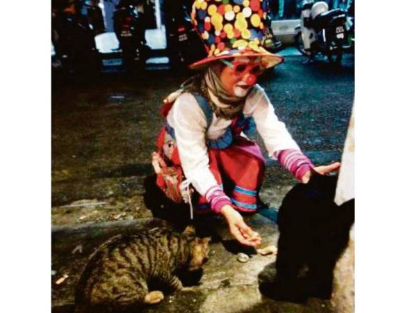 MAMA PINKY sanggup melakukan kerja sampingan sebagai badut demi mencari duit poket untuk menyara puluhan kucing jalanan dan peliharaan. Foto: BERNAMA