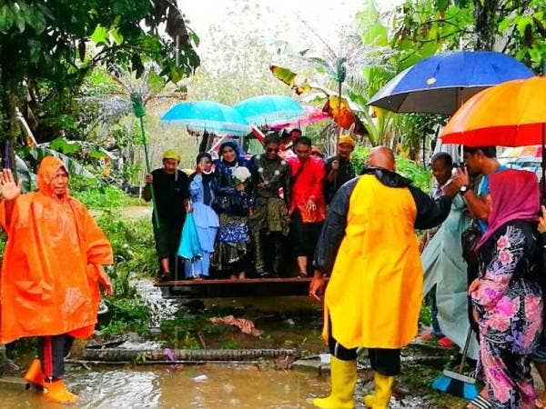 Pasangan raja sehari, Mohd Abdul Rozaid dan Nor Afiqah diarak menggunakan backhoe sambil diiringi traktor serta lori ekoran hujan lebat.