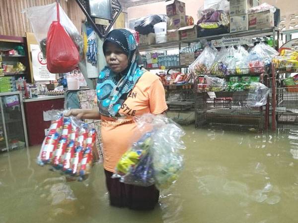 Fatimah mengangkat barangan yang boleh diselamatkan selepas kedai runcitnya dinaiki air.
