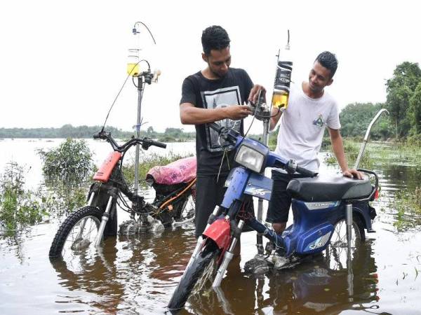 Muhammad Zakaria Mat Kail, 22, (kiri) dan abangnya Ikram Shahidi, 24, memeriksa karburetor yang telah diubahsuai bagi membolehkan motosikal meredah banjir dengan lancar ketika ditemui di Kampung Banggol.- Foto Bernama