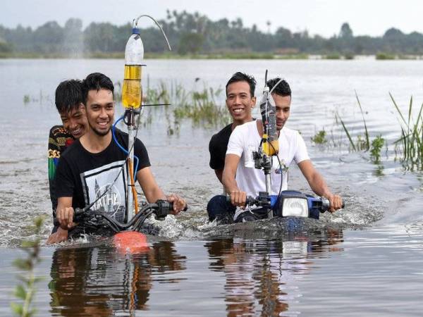 Muhammad Zakaria Mat Kail, 22, (kiri) dan abangnya Ikram Shahidi, 24, (kanan) menunggang motosikal telah diubahsuai yang mampu meredah banjir dengan lancar ketika ditemui di Kampung Banggol. - Foto Bernama
