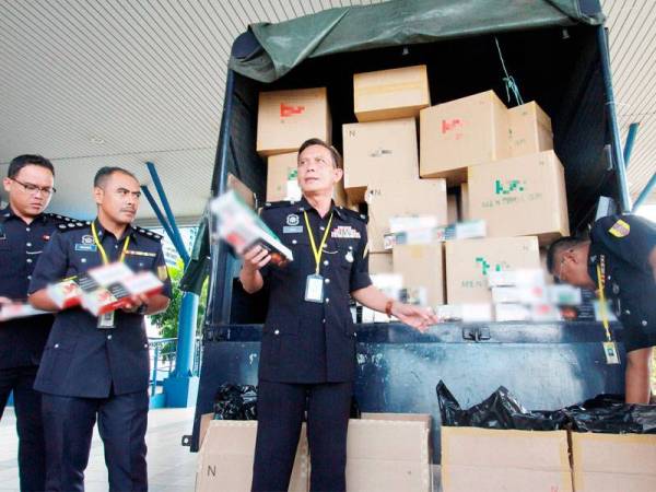 Kinsi (dua, kanan) menunjukkan rokok yang dirampas pelbagai jenama tidak bercukai bernilai RM1,453,500 dalam Op Libas di sebuah gudang di Batu Kitang. Foto: Bernama