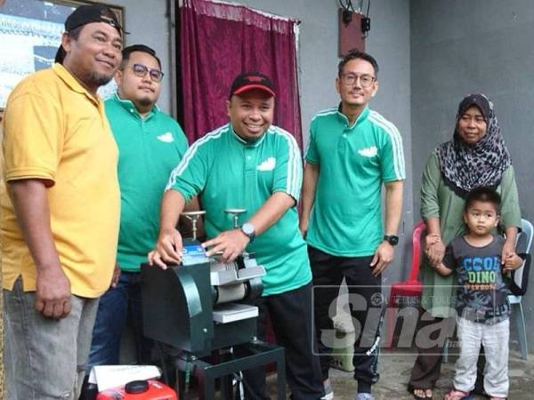 Abdul Halim (dua dari kiri) menyerahkan mesin memproses air tebu kepada Muhammad (kiri) di Kampung Telok Mas, Melaka.