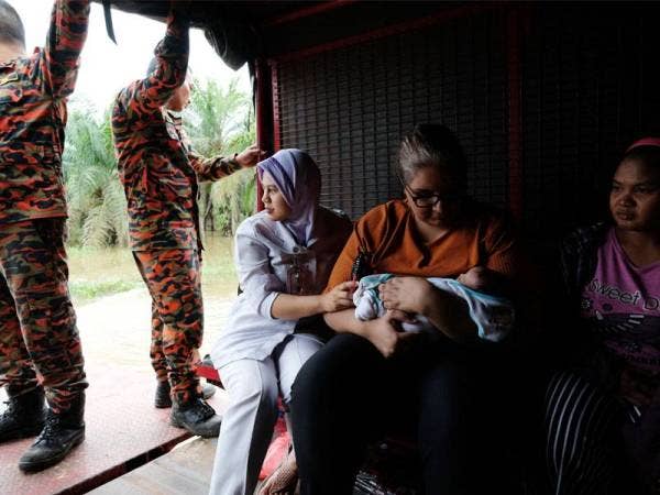 Doktor Klinik Ke, ihatan Tanjung Gemok, Dr Monysyha Atri (dua dari kanan) meriba bayi berumur 21 hari Nor Syakina Osman ketika keluar daripada kawasan banjir bersama ibu bayi Rohayani Ali, 27, menggunakan trak JBPM Rompin hari ini. -Foto Bernama