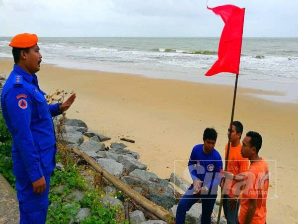 Anggota APM Pasir Puteh menaikkan bendera merah sebagai tanda amaran supaya orang ramai menjauhi kawasan pantai.