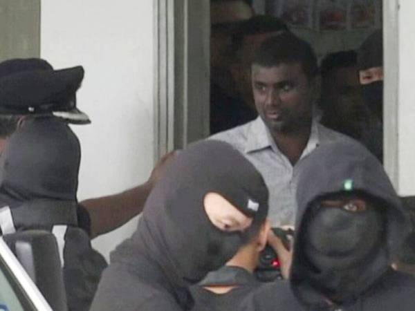 Saminathan diiringi anggota polis sebelum dibawa menaiki van polis meninggalkan pekarangan Mahkamah Sesyen Ayer Keroh.