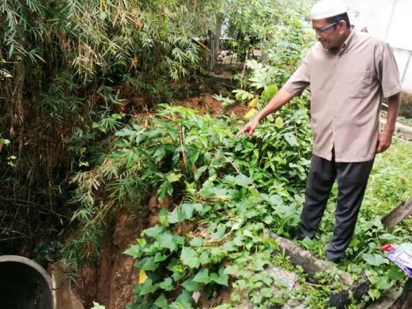 Abd Rahim menunjukkan antara kawasan tebing di belakang rumahnya yang runtuh di Kampung Felda LBJ semalam.