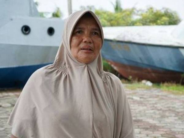 Saudah membelakangi dua kapal yang tersadai di hadapan rumahnya selepas dihanyutkan tsunami yang berlaku 15 tahun dahulu. - BBC Indonesia