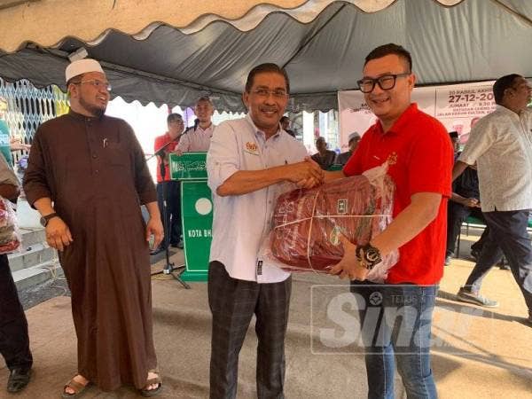Takiyuddin (tengah) menyerahkan beg sekolah kepada wakil penerima DUN Kota Lama pada program Back To School, Gunting Rambut Percuma Antara Kaum anjuran Lajnah Perpaduan Nasional Pas Kawasan Kota Bharu.
