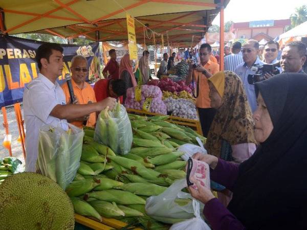 Pengerusi LKIM, Muhammad Faiz Fadzil (kiri) menjual jagung di bawah harga pasaran pada Program Bazar Peduli Rakyat di Kampung Pelet hari ini. Turut kelihatan, Ishak (dua dari kiri).- Foto Bernama