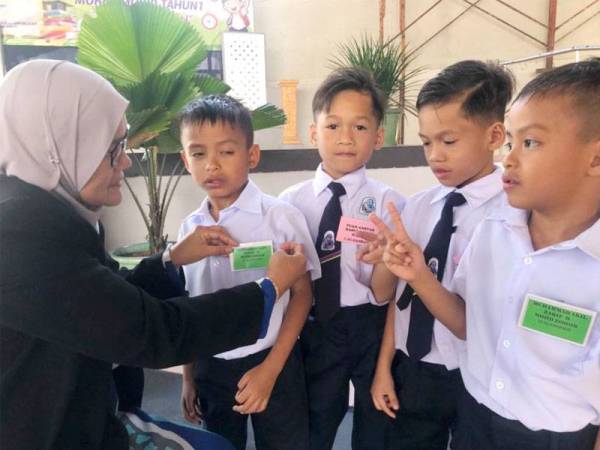 Faridah (kiri) membantu membetulkan tag nama Muhammad Akif Zikry sambil diperhatikan Tuan Amsyar Rasul, Tuan Ammar Rasul dan Muhammad Akil Zarif.