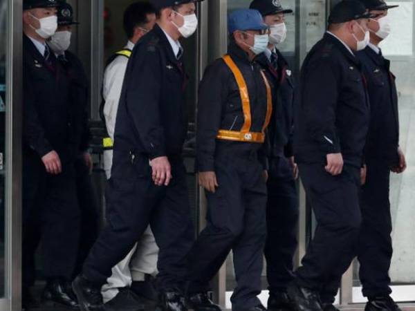 Ghosn memakai topi biru dan penutup muka selepas dibenarkan diikat jamin.