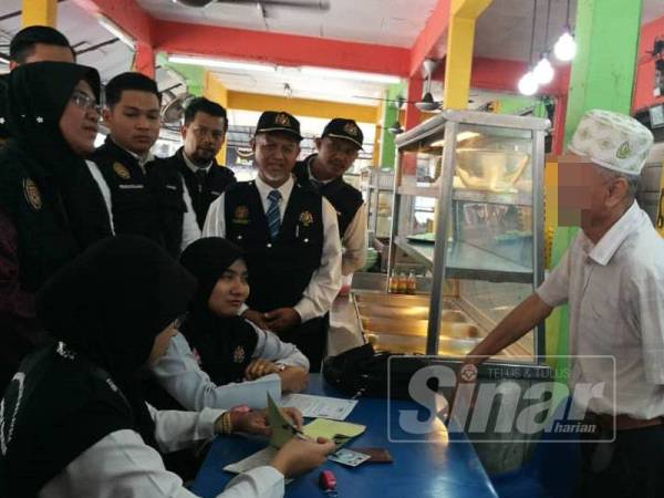 Nor Azimi (berdiri, kiri) sedang menyoal siasat salah seorang peniaga yang dikesan tidak mempamerkan papan tanda larangan merokok di kedai makan miliknya sempena Ops Larangan Merokok pagi tadi.