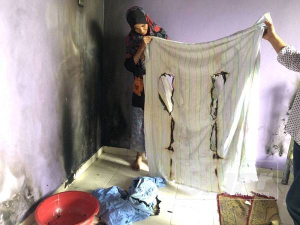 Ropeah (kiri) menunjukkan kesan kain yang terbakar di rumah baharu yang didiami keluarga itu.