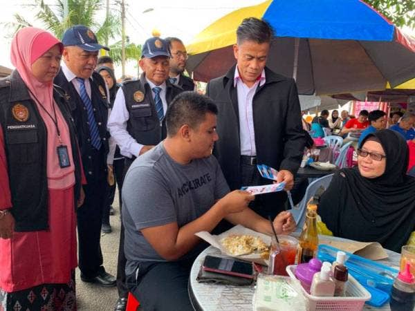 Dr Zaini (berdiri) memberikan penerangan berkaitan penguatkuasaan larangan merokok di kedai makan kepada pelanggan Ayang Café pada hari pertama ia dikuatkuasa.