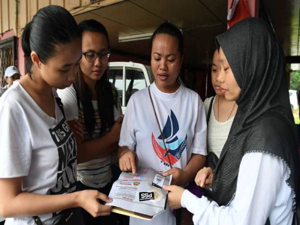 Seorang penduduk Kampung Kelatuan Batu Lapan Normilah Salleh, 38, (kanan) bersama rakan-rakan sekampung melihat risalah mengandungi maklumat mengenai PSS sambil mendengar penerangan diberikan oleh salah seorang jentera kempen Parti Warisan Sabah di kampung tersebut hari ini. - Foto: Bernama