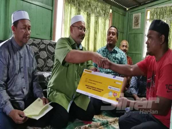 Wan Sukairi (dua kiri) menyerahkan bantuan faedah pengurusan jenazah dari Perkeso, kepada Badrul Hisham.