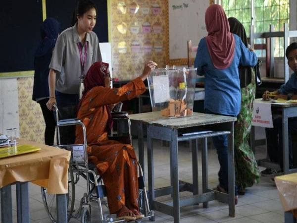 Petugas SPR membantu seorang pengundi orang kurang upaya ketika mengundi tanggungjawab mengundi bagi PRK Kimanis di SK Kimanis dekat sini hari ini.- Foto Bernama