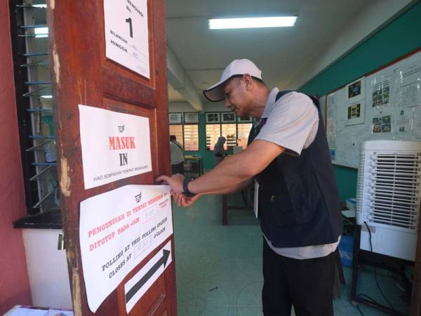 Petugas Suruhanjaya Pilihan Raya menanggalkan tanda arah pada pintu saluran mengundi sebaik sahaja waktu mengundi tamat jam 5 petang di Pusat Pengundian Pilihan Raya Kecil Parlimen Kimanis di Sekolah Menengah Membakut hari ini. - Foto Bernama
