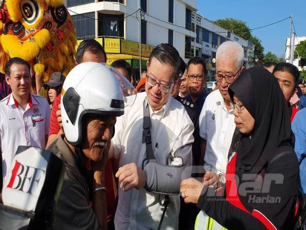 Guan Eng (tengah) memberi topi keledar baharu kepada seorang penunggang motosikal sempena kempen keselamatan jalan raya pagi tadi.
