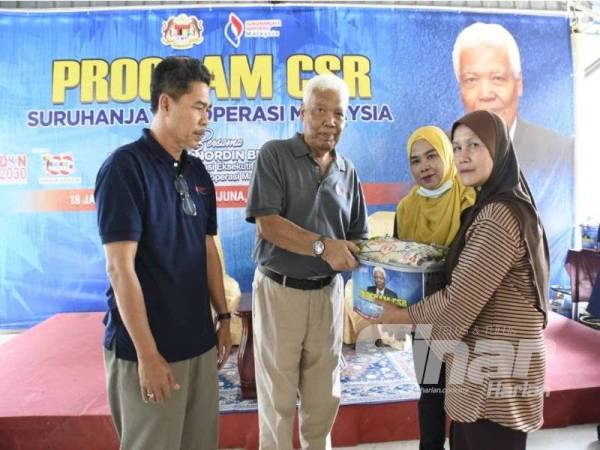 Nordin (dua dari kiri) mengagihkan barangan makanan harian kepada penerima di Pulau Sri Tanjung, Tumpat semalam.
