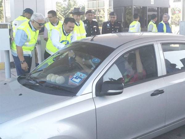 Ahmad Fuad (kiri) menyampaikan cenderahati kepada pengguna LATAR pada Kempen Keselamatan Jalan Raya di Plaza Tol Ijok di sini hari ini.