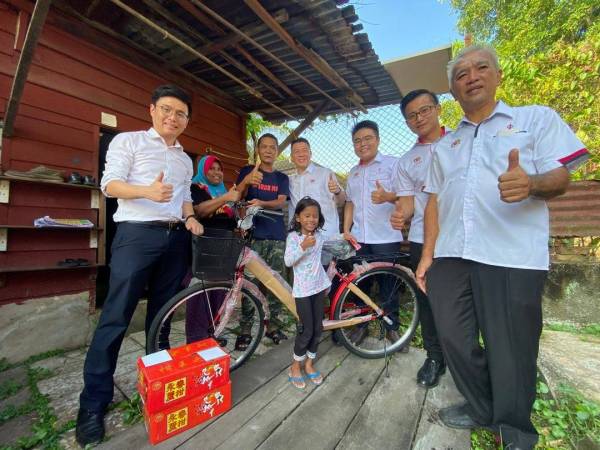 Kor Ming (tengah) bersama Kah Leong (tiga dari kanan) menyampaikan bantuan basikal dan wang tunai berserta limau mandarin kepada Azmi Yusof yang tinggal di Pasir Bedamar baru-baru ini.