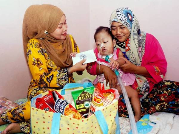 Pengerusi Sahabat Charity Balqish (SCB) Rukiza Abu Bakar (kiri) menyampaikan sumbangan kepada Nur Auni Husnina Mohamad Radzi, 2, yang mengidap masalah paru-paru dan jantung berlubang kronik di rumahnya di Kampung Sena, Padang Temak, hari ini. - Foto Bernama