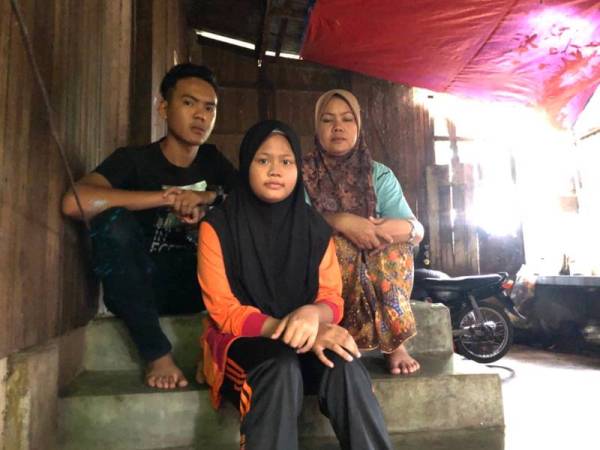 Dahalia (kanan), Harithah Zayani dan Harith Denial duduk di tangga dapur rumah mereka yang dindingnya hampir roboh akibat reput dan dimakan anai-anai.