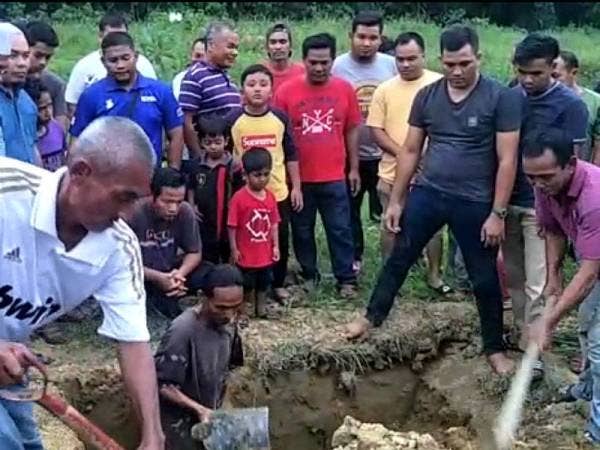 Mohd Taquddin (kiri, berbaju hitam) melihat proses pengebumian anaknya