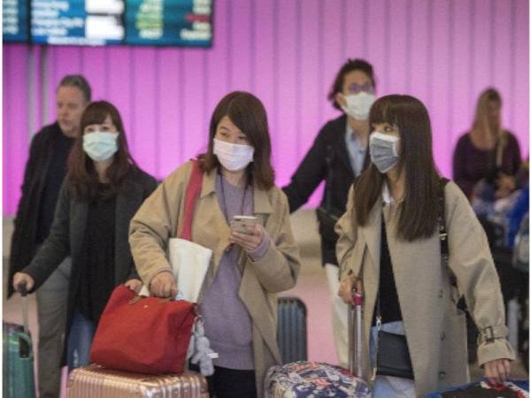 Penumpang memakai topeng muka sebagai langkah perlindungan terhadap penularan koronavirus ketika tiba di Lapangan Terbang Antarabangsa Los Angeles, California. - Foto: AFP