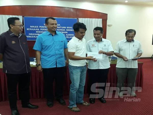 Mohd Fadzli (dua dari kiri) dan Zulkifli (kiri) menyaksikan penyerahan bantuan khas kepada mangsa kebakaran yang disampaikan Mazlan pada majlis penyerahan bantuan dan pengumuman khas kerajaan Persekutuan kepada mangsa kebakaran di Pulau Tioman di Tanjung Gemok di sini.