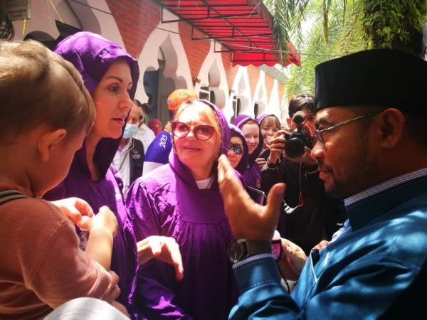 Mujahid (kanan) beramah mesra dengan pelancong selepas mengagihkan pembersih tangan percuma di Masjid Jamek Sultan Abdul Samad di sini hari ini.