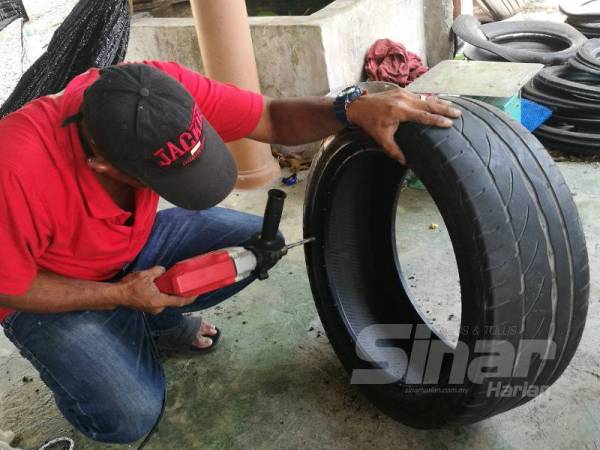 Noor Azizi menebuk lubang pada tayar bagi membolehkan tali dipasang 