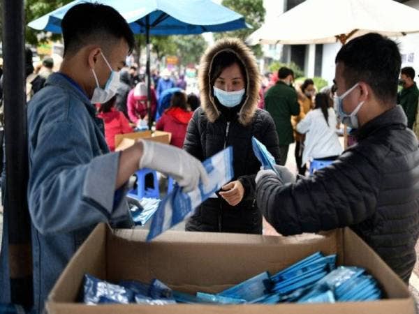 Penduduk Vietnam (tengah) menerima topeng muka percuma di Hanoi hari ini. - Foto AFP