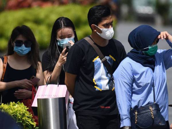 Orang ramai memakai topeng muka menunggu di persimpangan pejalan kaki di Singapura. Foto: AFP